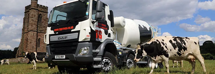 A cow-patterned TG Concrete mixer truck with cattle in front of a stone tower